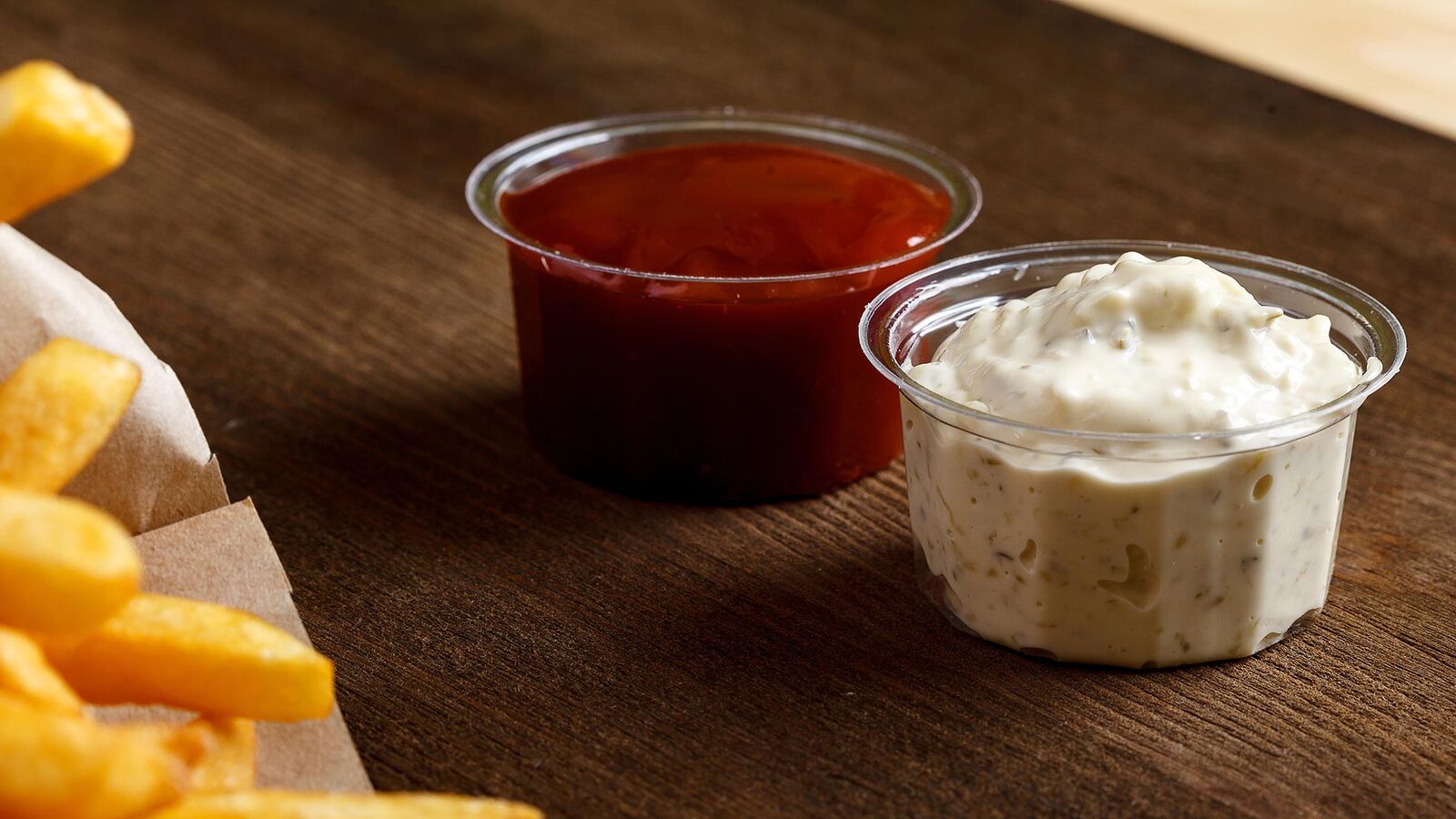 Prohibited: Dips in disposable plastic packaging On a table next to a bag of chips are dip bowls with ketchup and mayonnaise