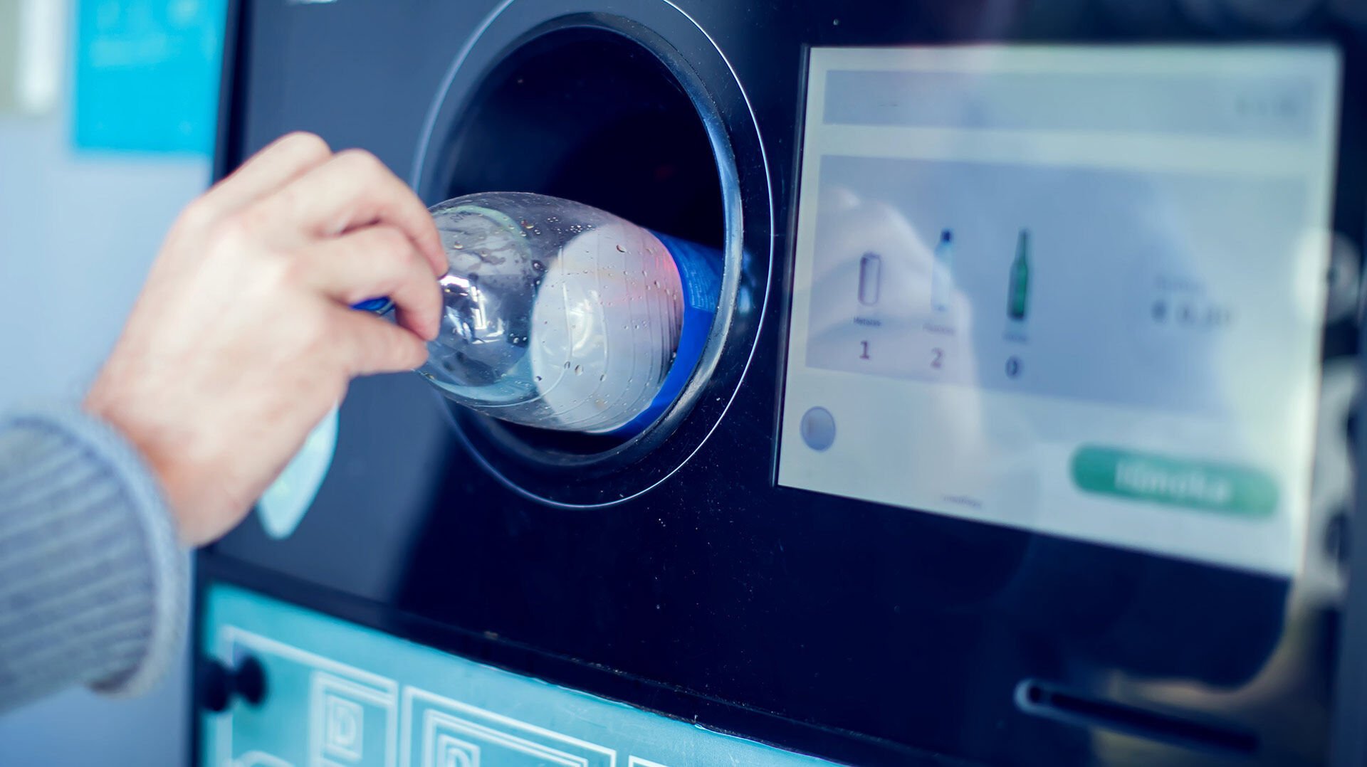 Deposit systems A hand pushes a transparent plastic water bottle into a deposit machine