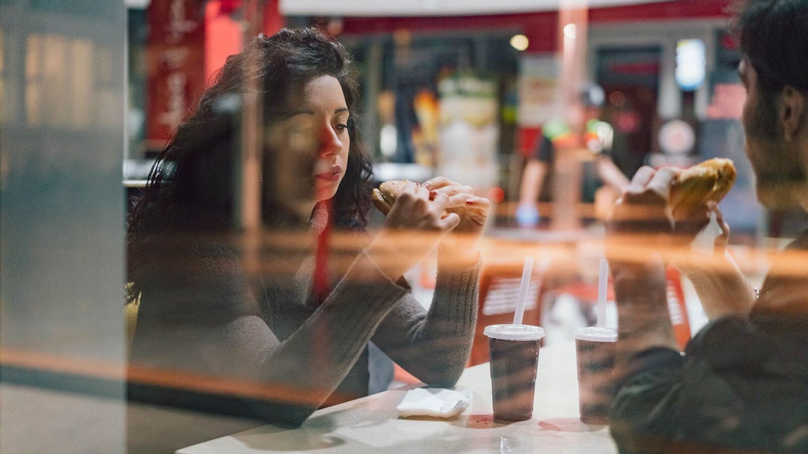 Prohibited: Disposable food packaging for on-site consumption A couple is sitting at a table in a fast food restaurant eating a burger; there are drinks in disposable packaging on the table