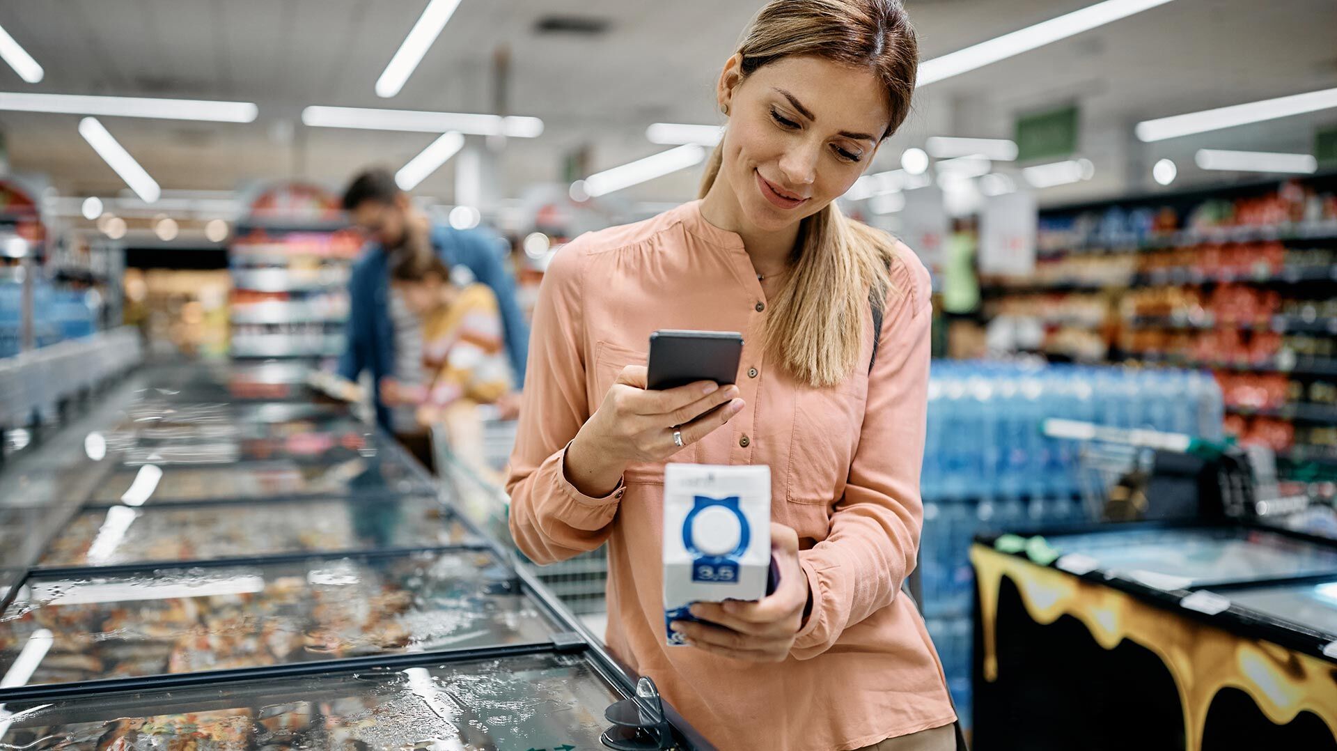 Labeling requirements A smiling woman scans the QR code on a milk carton with her smartphone in the supermarket