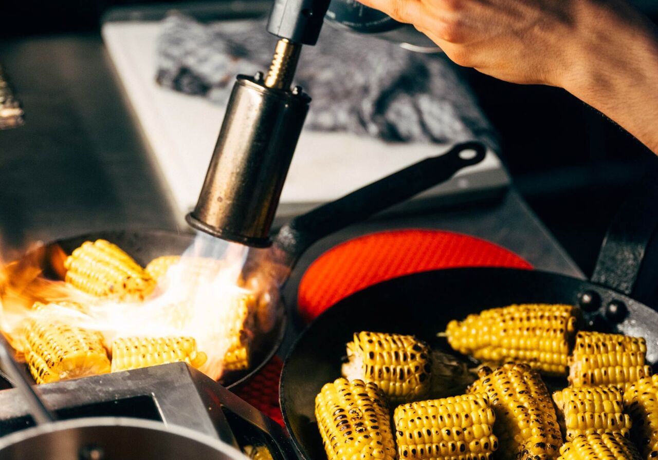 Cook flambéing corn on the cob in the pan