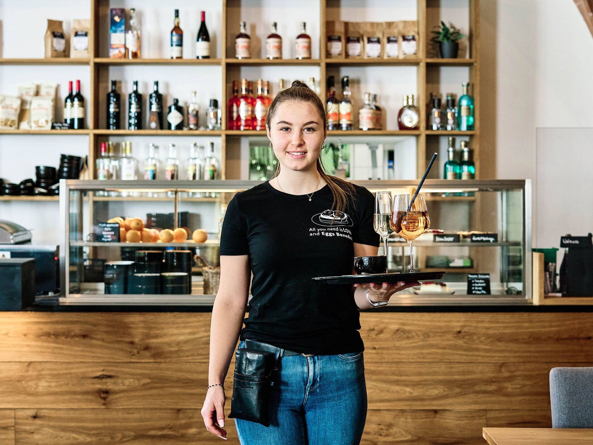 Staff shortages in the foodservice industry – how to find employees! A waitress stands in front of the counter of a restaurant with a tray of drinks