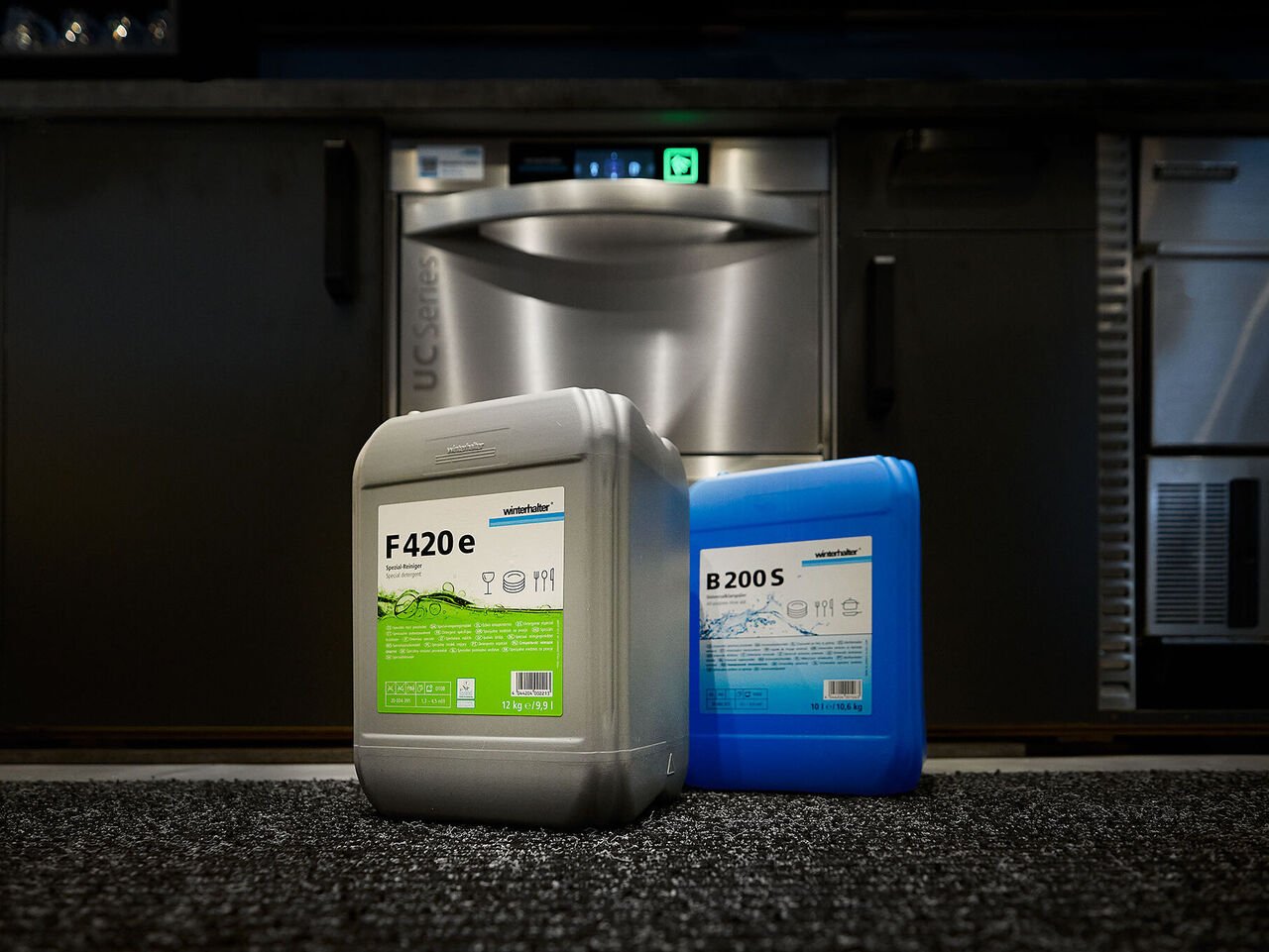 Conseils pour prévenir la corrosion du verre : utilisez des produits chimiques pour le lavage du verre Deux bidons contenant des produits lessiviels pour le lavage du verre et un dispositif de dosage à côté d'un lave verres comme protection contre la corrosion du verre