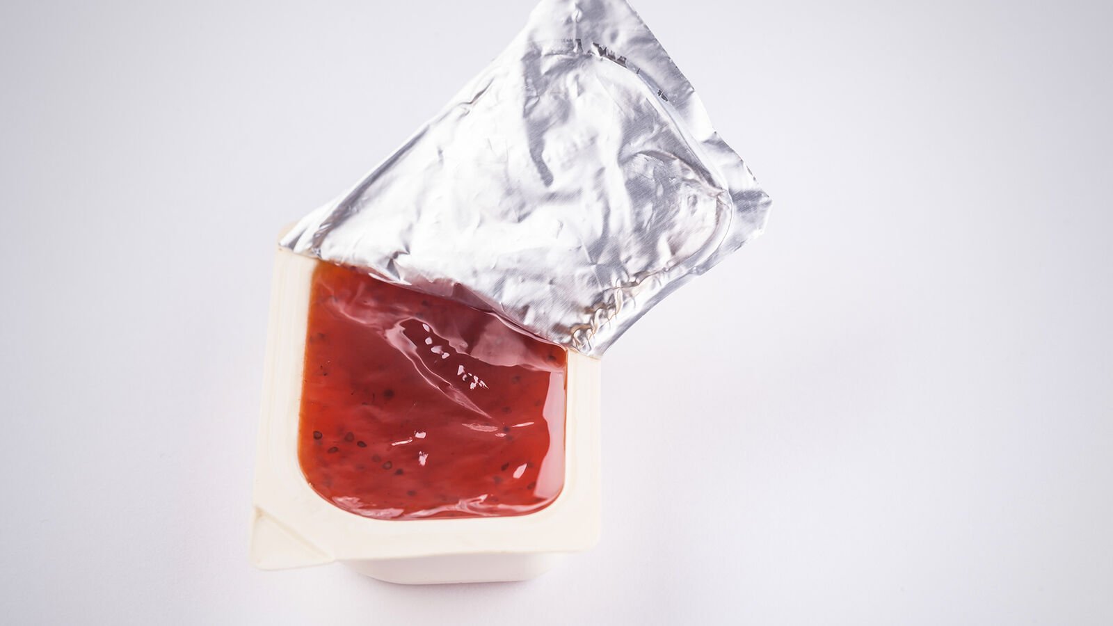 Prohibited: Mini portions of jam in disposable plastic packaging An opened mini portion of jam in plastic packaging