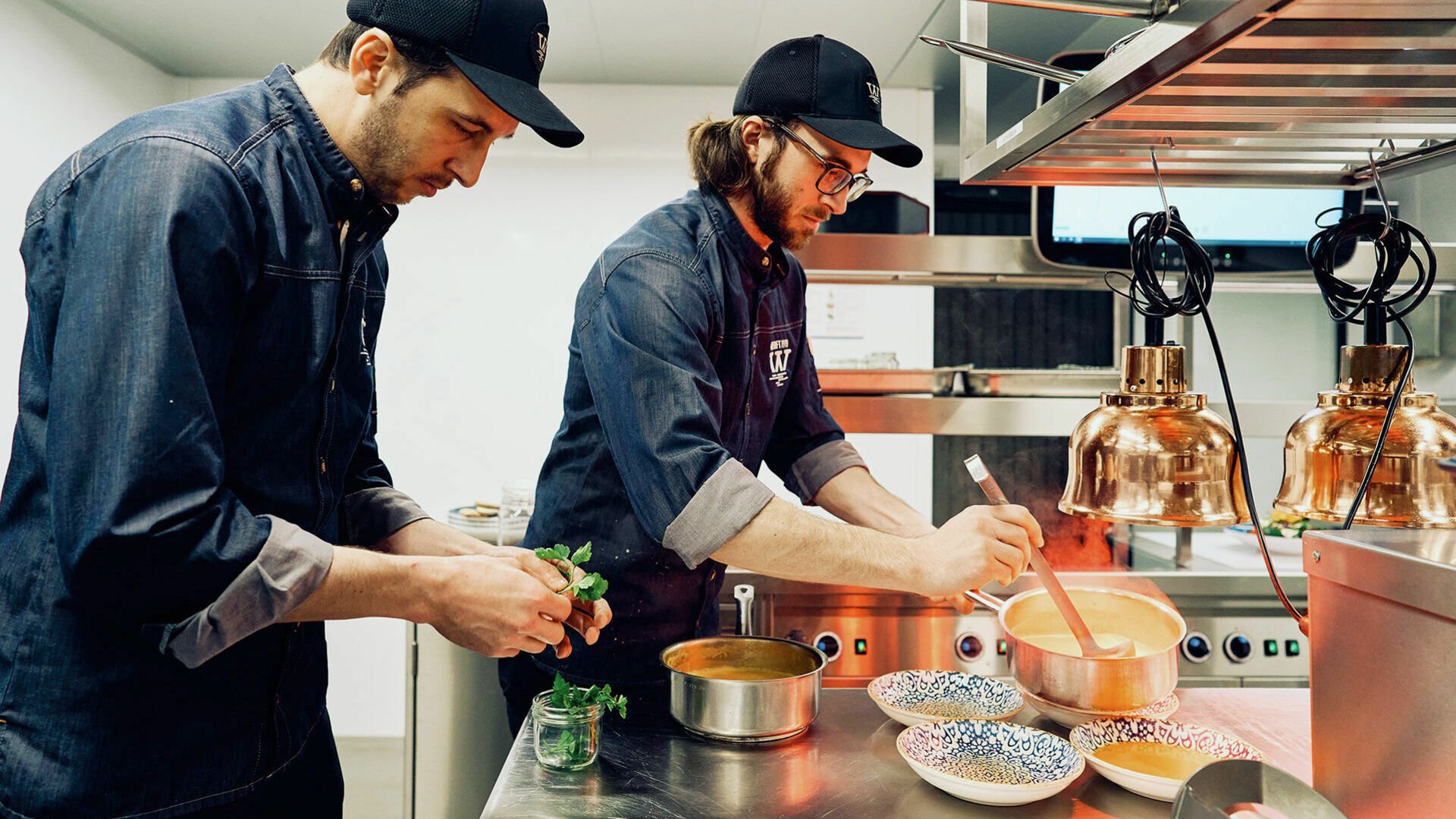 Energiespar-Tipps: Kochen und Garen Zwei Köche nehmen fertig gekochte Beilagen von einem Blech und richten Gerichte auf den Tellern an