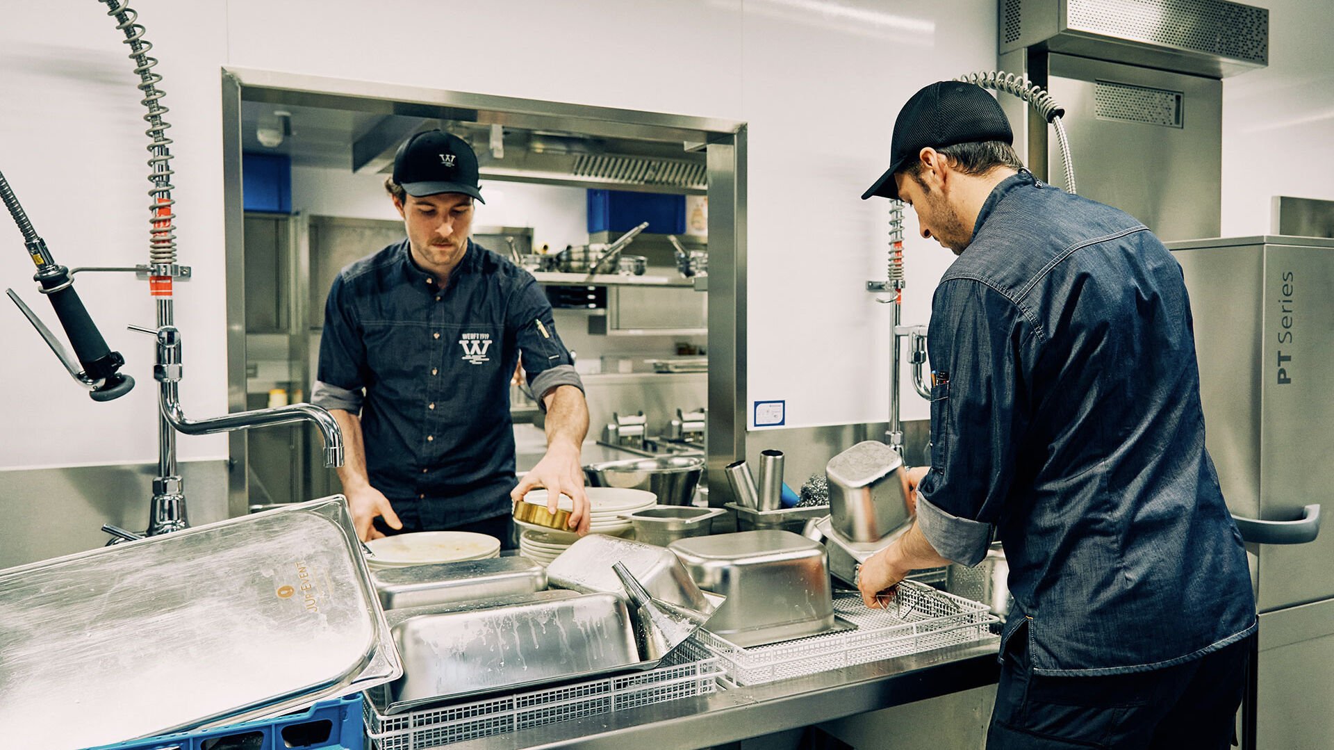 Energiespar-Tipps: rund ums Spülen Zwei Mitarbeiter sammeln in einer Gastro-Küche Geschirr und GN-Behälter für das Spülen