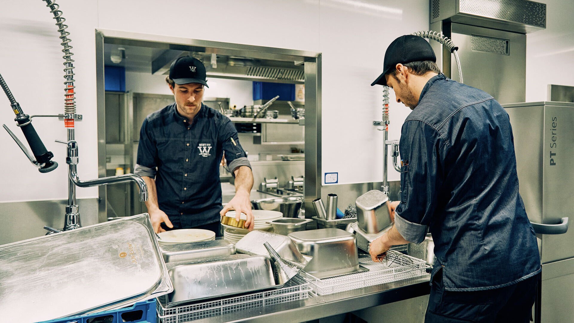 Energiespar-Tipps: rund ums Spülen Zwei Mitarbeiter sammeln in einer Gastro-Küche Geschirr und GN-Behälter für das Spülen