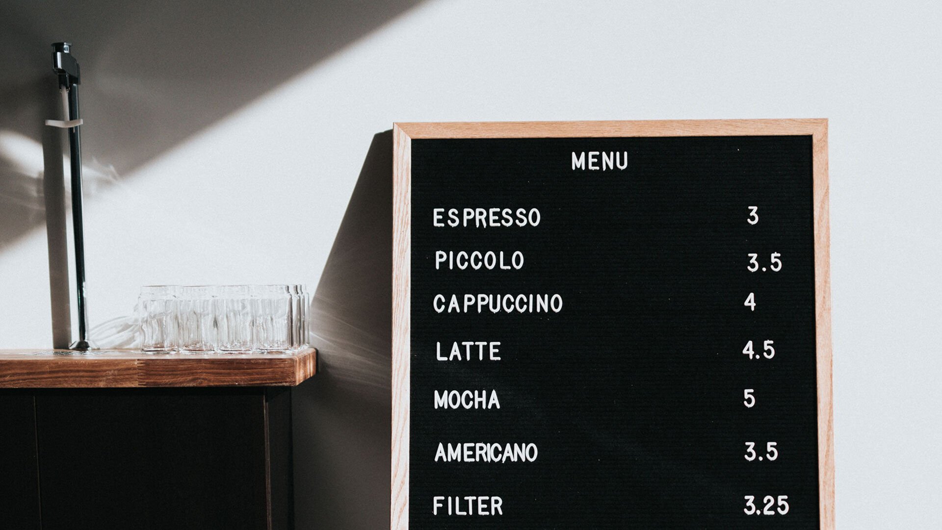 Preise clever angeben! In einem gastronomischen Betrieb lehnt neben einem Regal eine Tafel mit Kaffeespezialitäten und Preisen