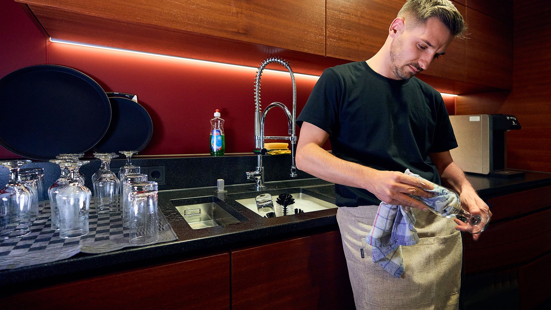 Inconvénient du lavage des verres à la main : impopulaire et démotivant Un homme se tient à l'évier d'un comptoir de bar et polit un verre avec un chiffon sec à s'ennuyer