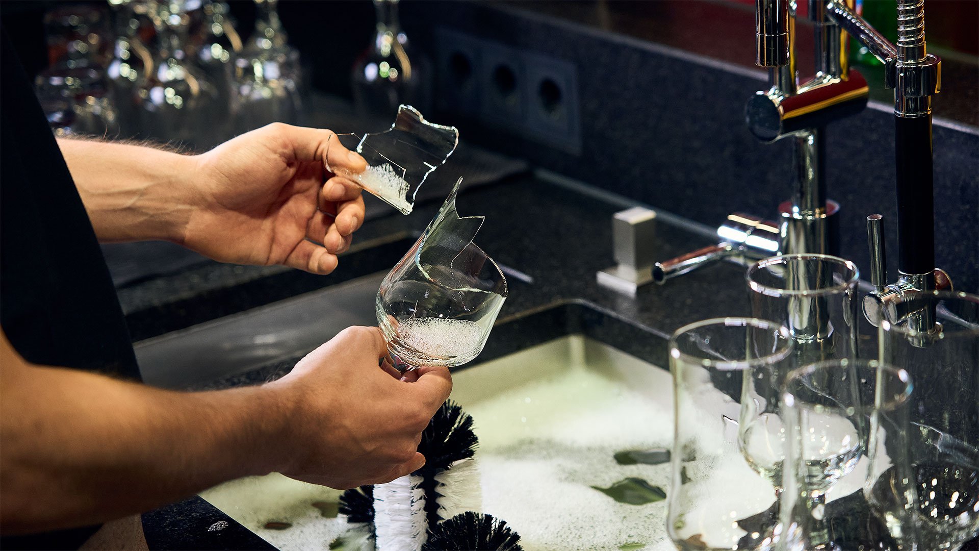Inconvénient de laver les verres à la main : risque élevé de blessure Un homme se tient devant l'évier d'un comptoir de bar et tient un verre de bière cassé et un éclat de verre dans ses mains
