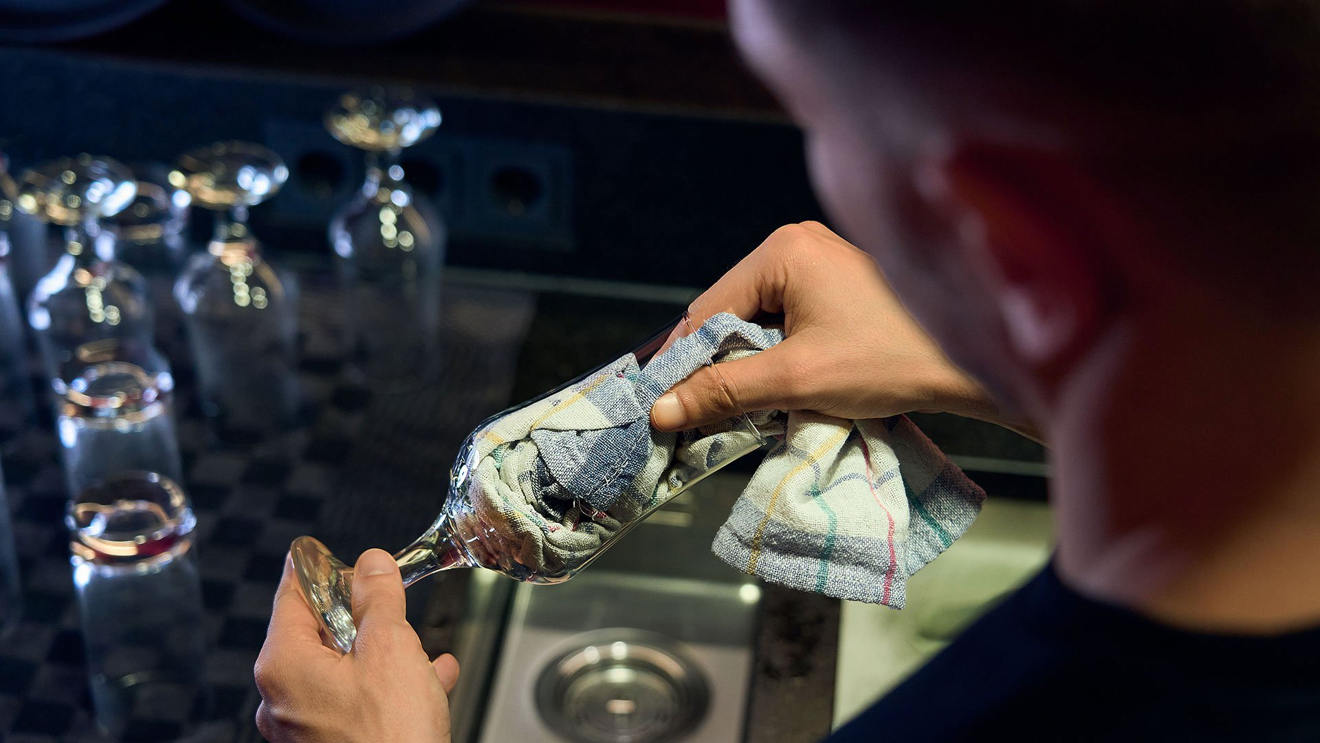 Nachteil beim Handspülen von Gläsern: Übertragung von Keimen Mann steht am Spülbecken einer Gastro-Theke und trocknet mit einem Poliertuch ein frisch gespültes Glas ab