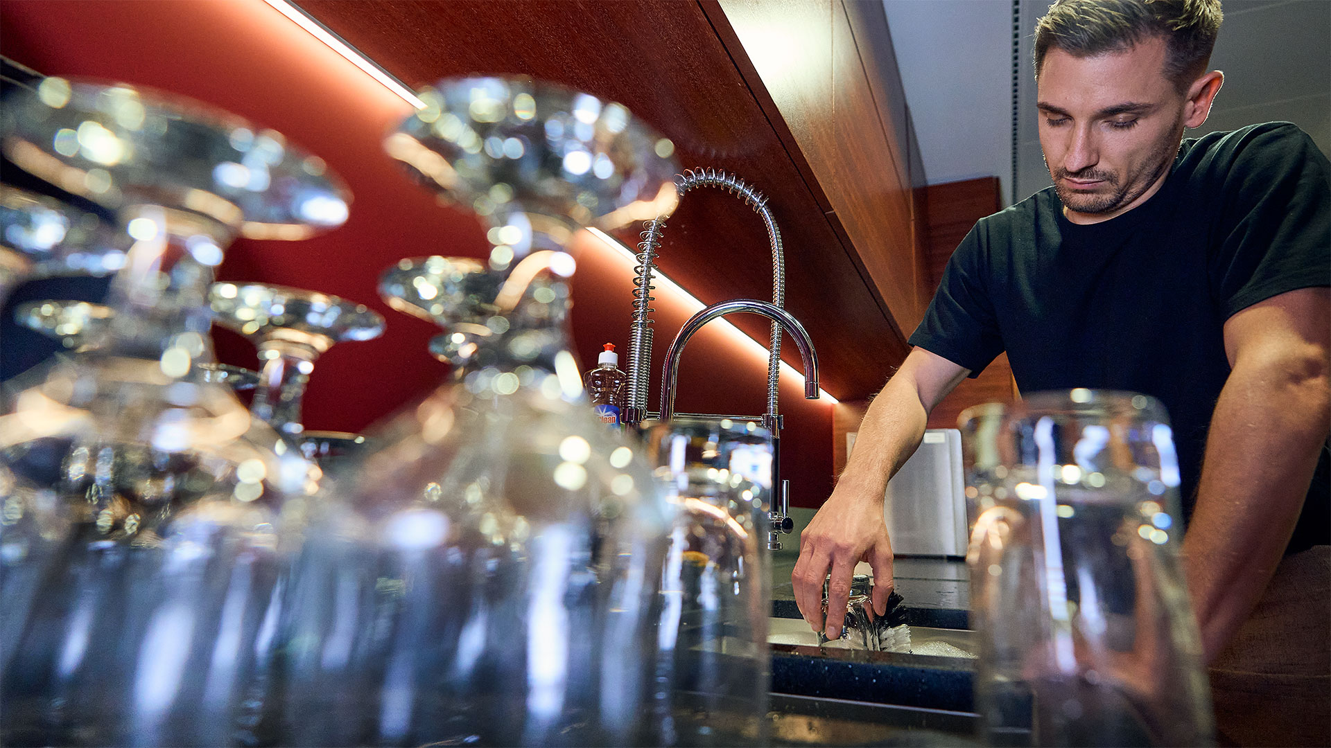 Nachteile beim Handspülen von Gläsern: hoher Zeitaufwand und hohe Kosten Mann steht am Spülbecken einer Gastro-Theke und stützt sich erschöpft mit einem Arm auf dem Rand des Beckens ab