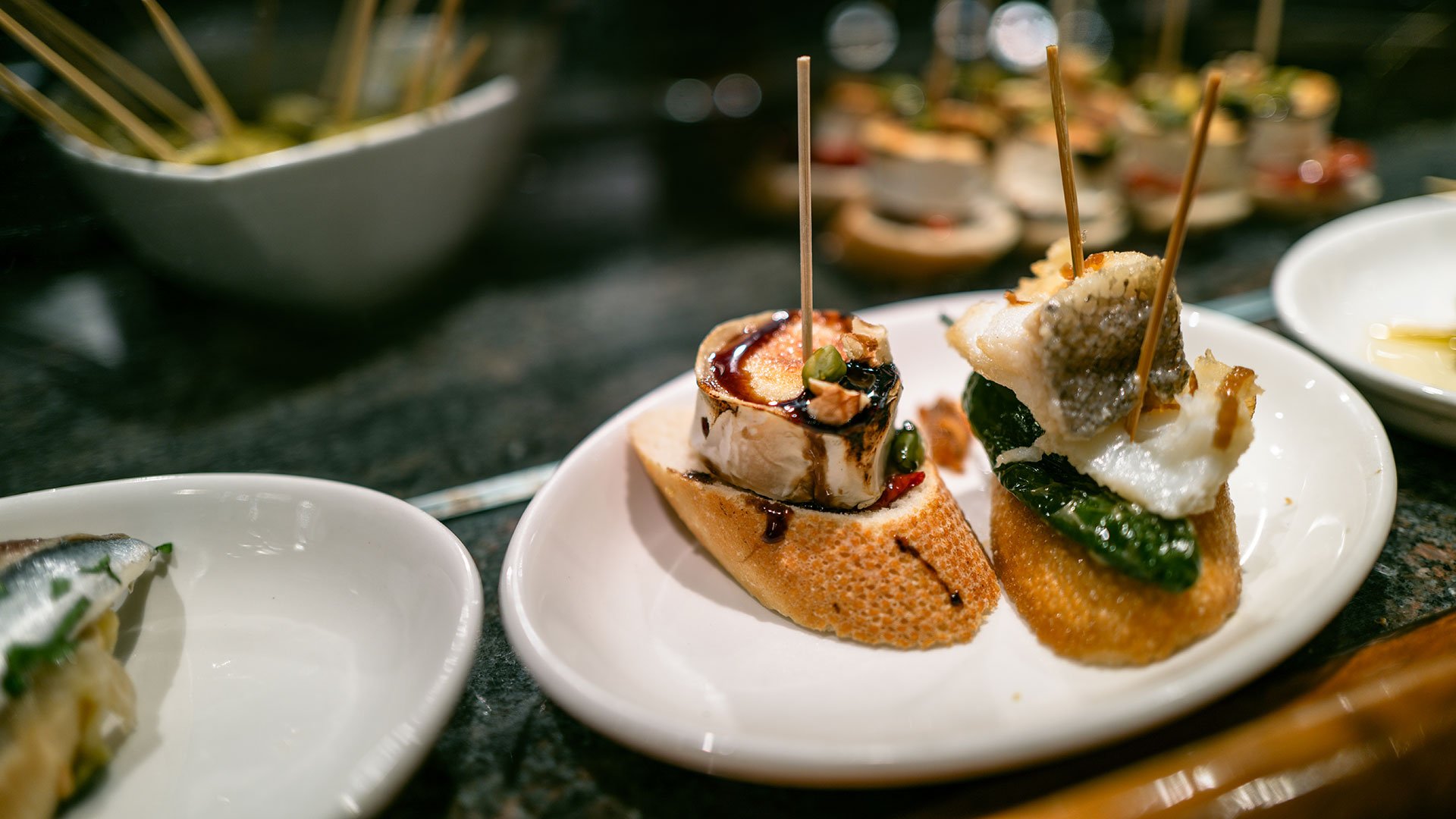 Tip 9: Always offer something new (How about Pintxos from the Basque Country?) Several white plates of pintxos from the Basque Country are laid out on the table of a restaurant