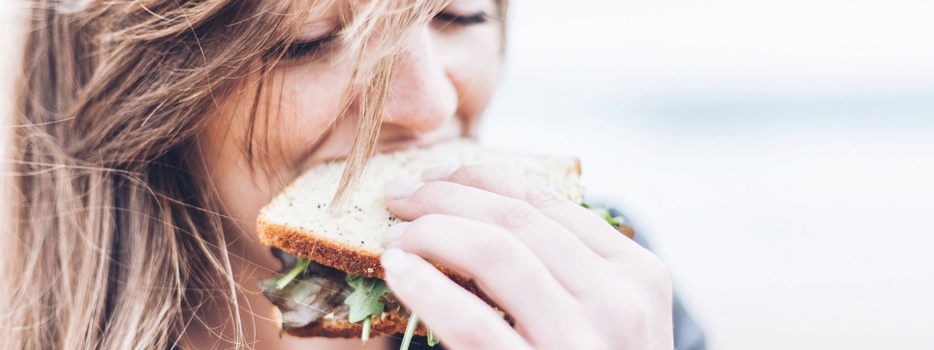 Plant-based food is becoming more and more popular! A woman with blonde hair gleefully takes a bite of a sandwich topped with salad